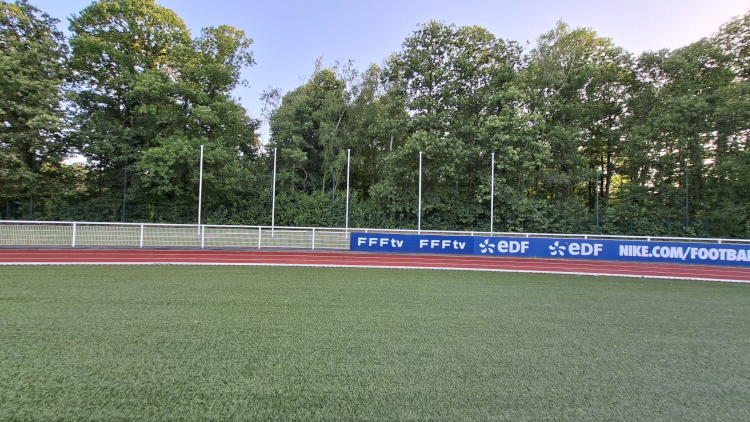 Alignement parfait des mâts en bordure de piste d'athlétisme — vue de profil et vue depuis le terrain, avec les panneaux partenaires FFF en arrière-plan. Vue depuis le terrain — mâts + panneaux FFFtv / EDF / Nike