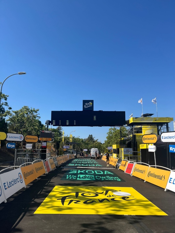 La zone d'arrivée du Tour de France 2026 en cours d'installation — marquage SKODA au sol, signalétique E.Leclerc, barriérage Continental. Toute la signalétique visible est installée et conforme à la charte officielle par les équipes Doublet. Marquage au sol SKODA en cours — camion Doublet en arrière-plan