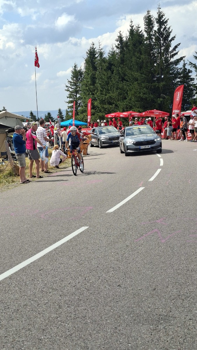 La zone d'activation "Le Virage Vittel" sur le Tour de France 2026 — barrières personnalisées, beach flags et parasols aux couleurs de la marque, déployés et installés par Doublet. Vue d'ensemble — zone Vittel avec barrières, beach flags et parasols, coureurs en arrière-plan